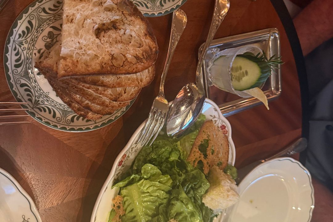 An overhead view of a table with sliced bread, a green salad with croutons, and a garnished drink.