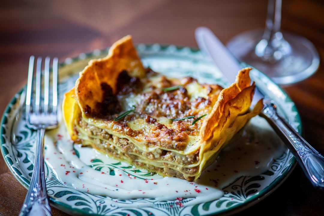 A layered slice of baked pasta with meat and melted cheese on a patterned plate.