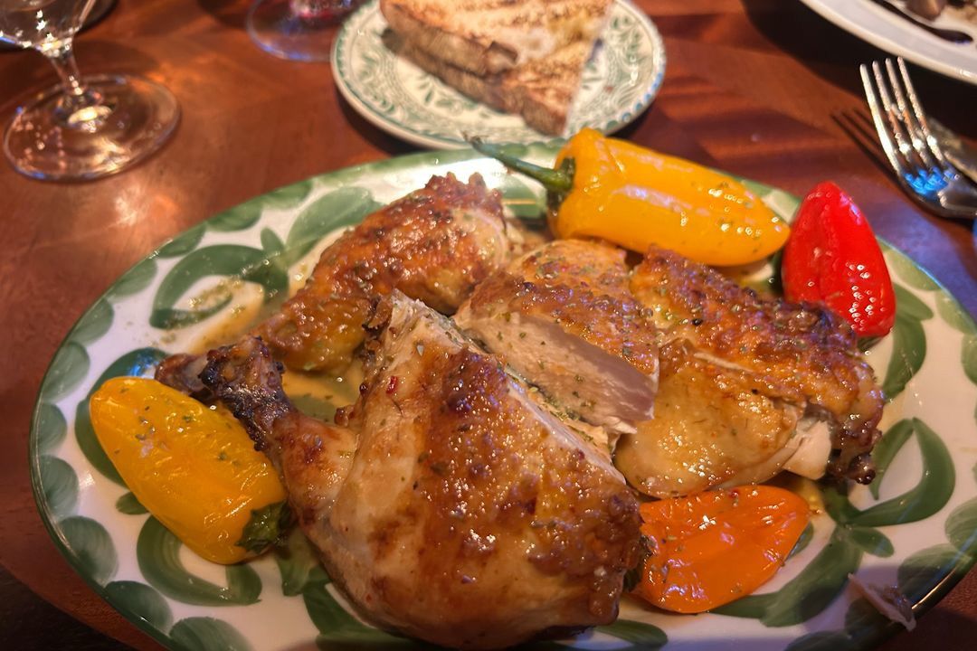 A sliced roast chicken with charred peppers on a decorative plate.