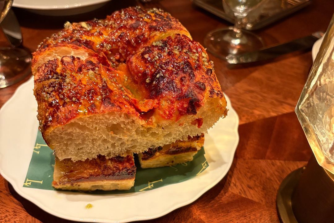 A thick slice of focaccia bread with a charred, cheesy top on a plate.
