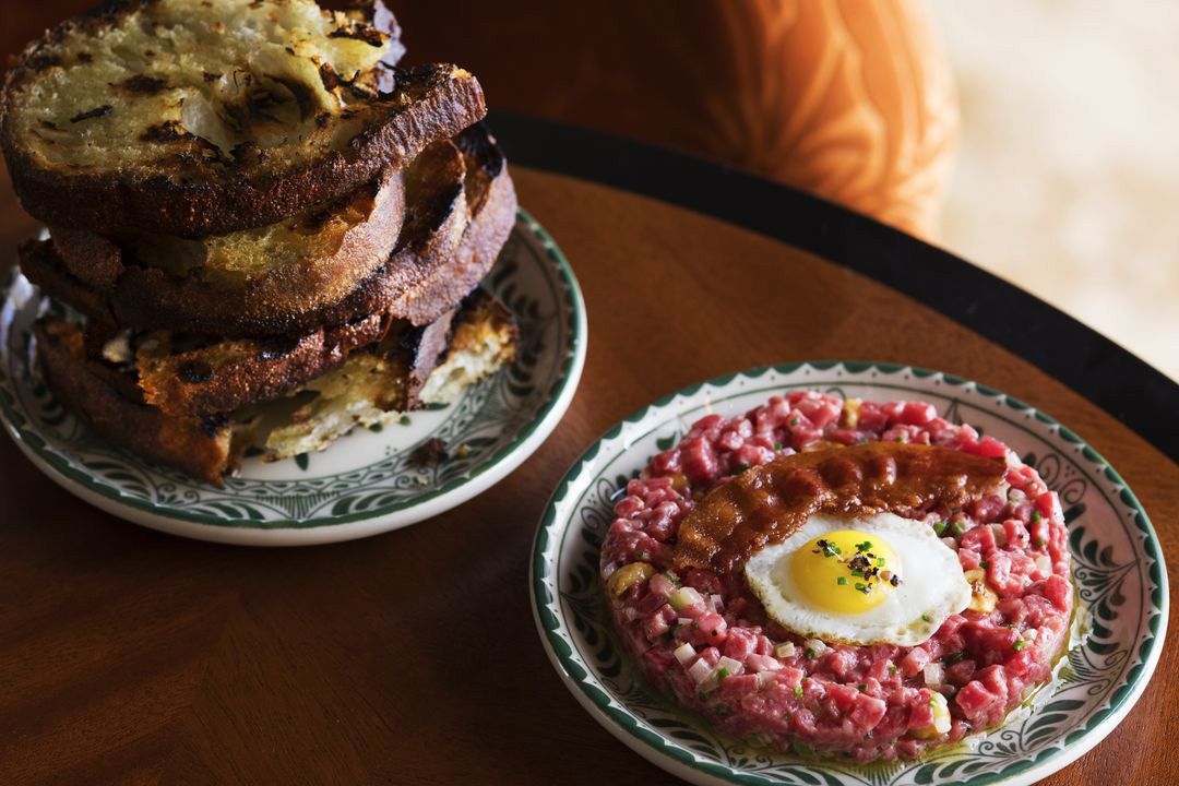 Steak tartare topped with a fried egg alongside a stack of grilled bread slices.