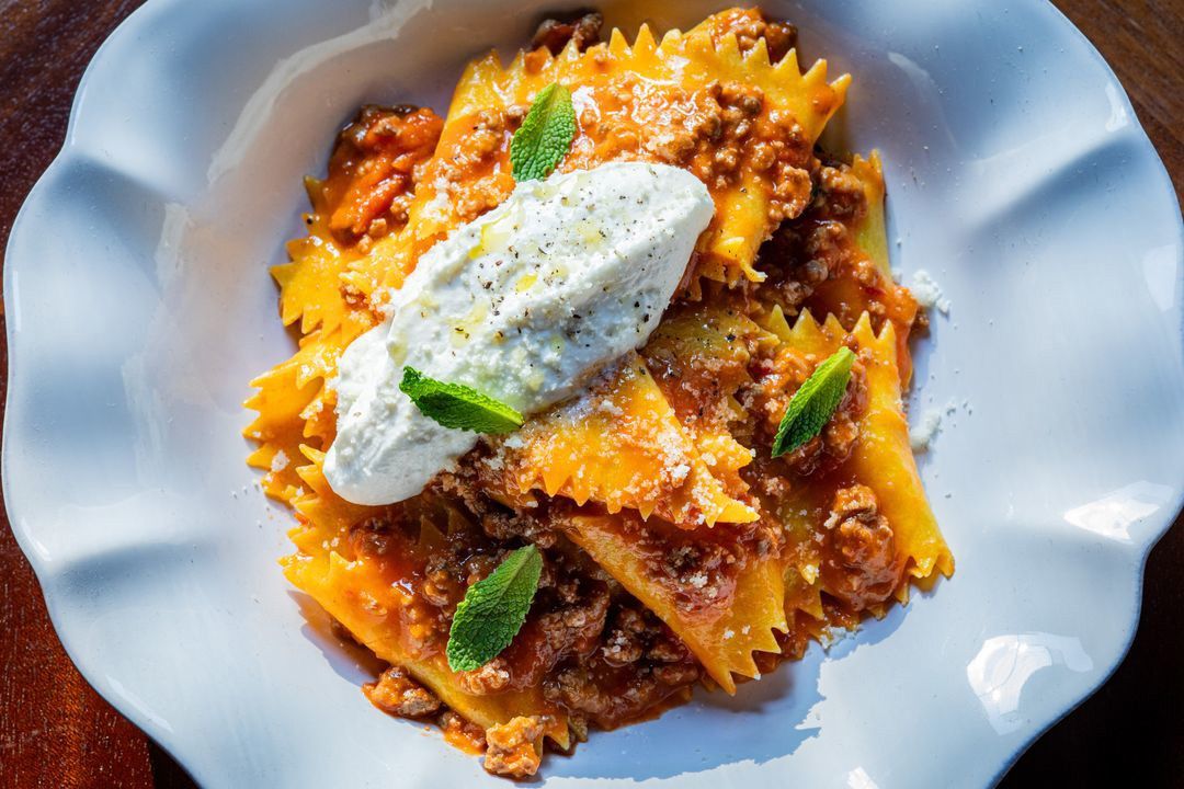 A pasta dish with meat sauce topped with a dollop of whipped cheese and mint leaves.