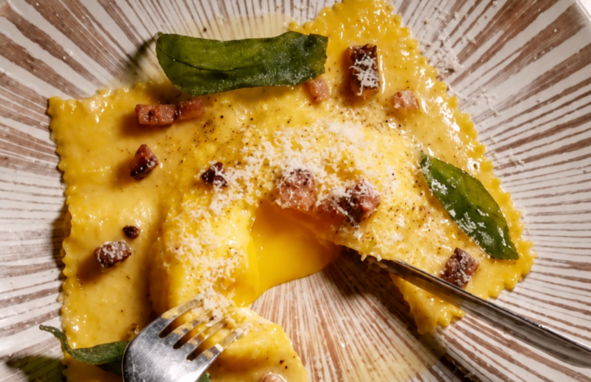 A pasta parcel with a runny egg yolk centre, topped with cured meat pieces, grated cheese and crisp sage leaves.