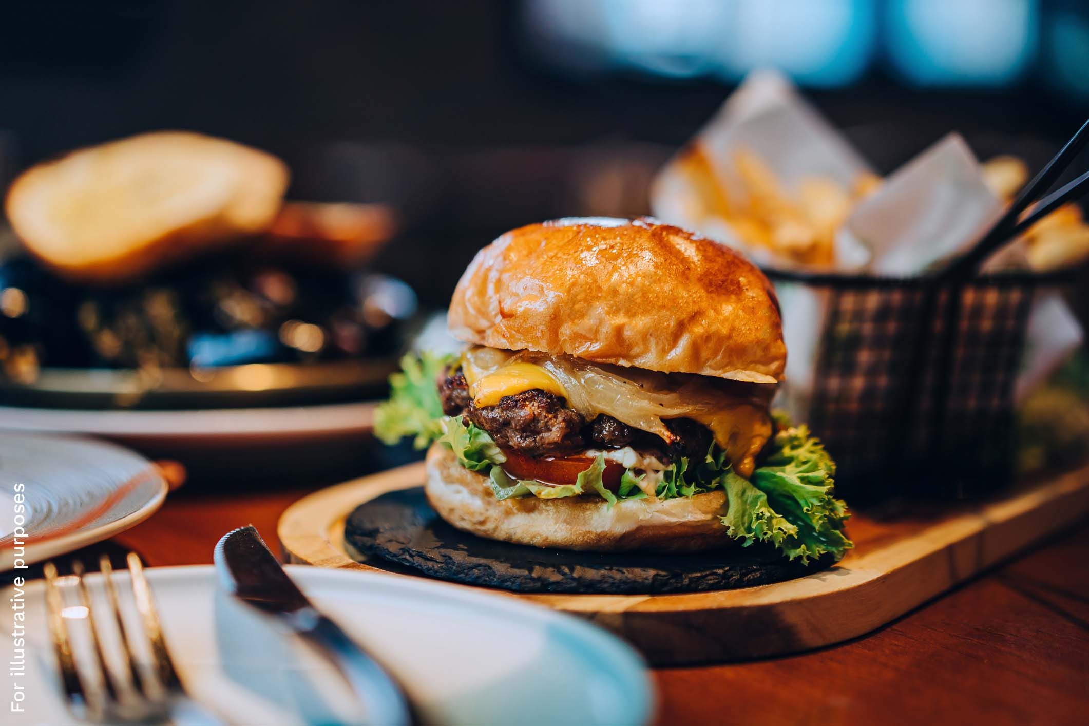 A burger with a beef patty, melted cheese, caramelised onion, lettuce, and tomato on a glazed bun, served with a side of fries.