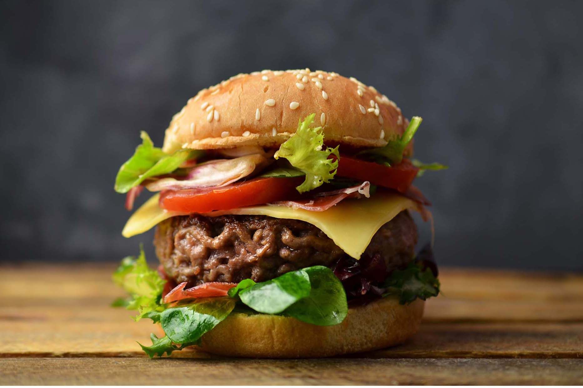 A burger with a beef patty, melted cheese, tomato, and lettuce on a sesame bun.