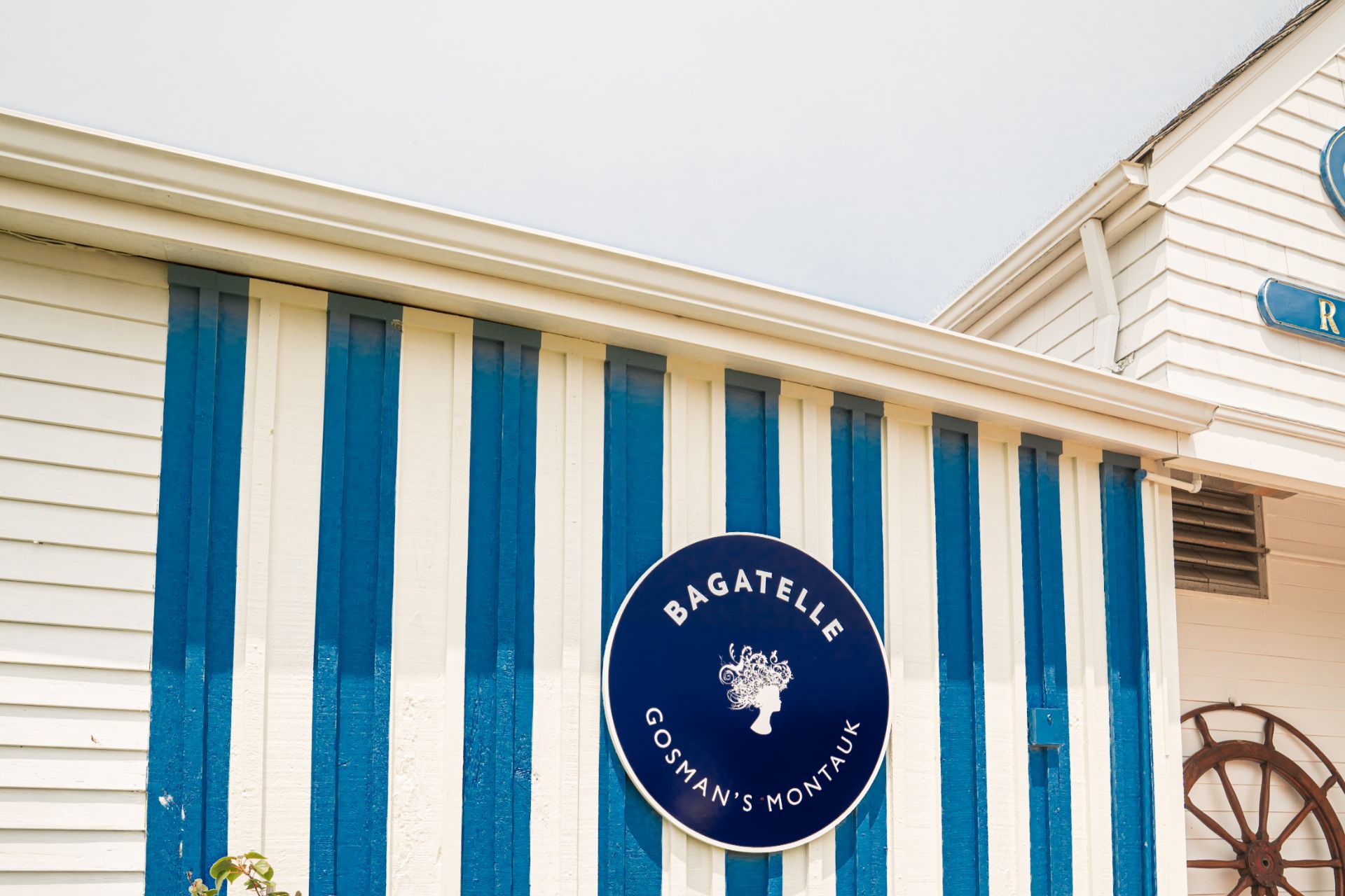 A circular sign reading Bagatelle Gosman's Montauk mounted on a blue and white striped building exterior.