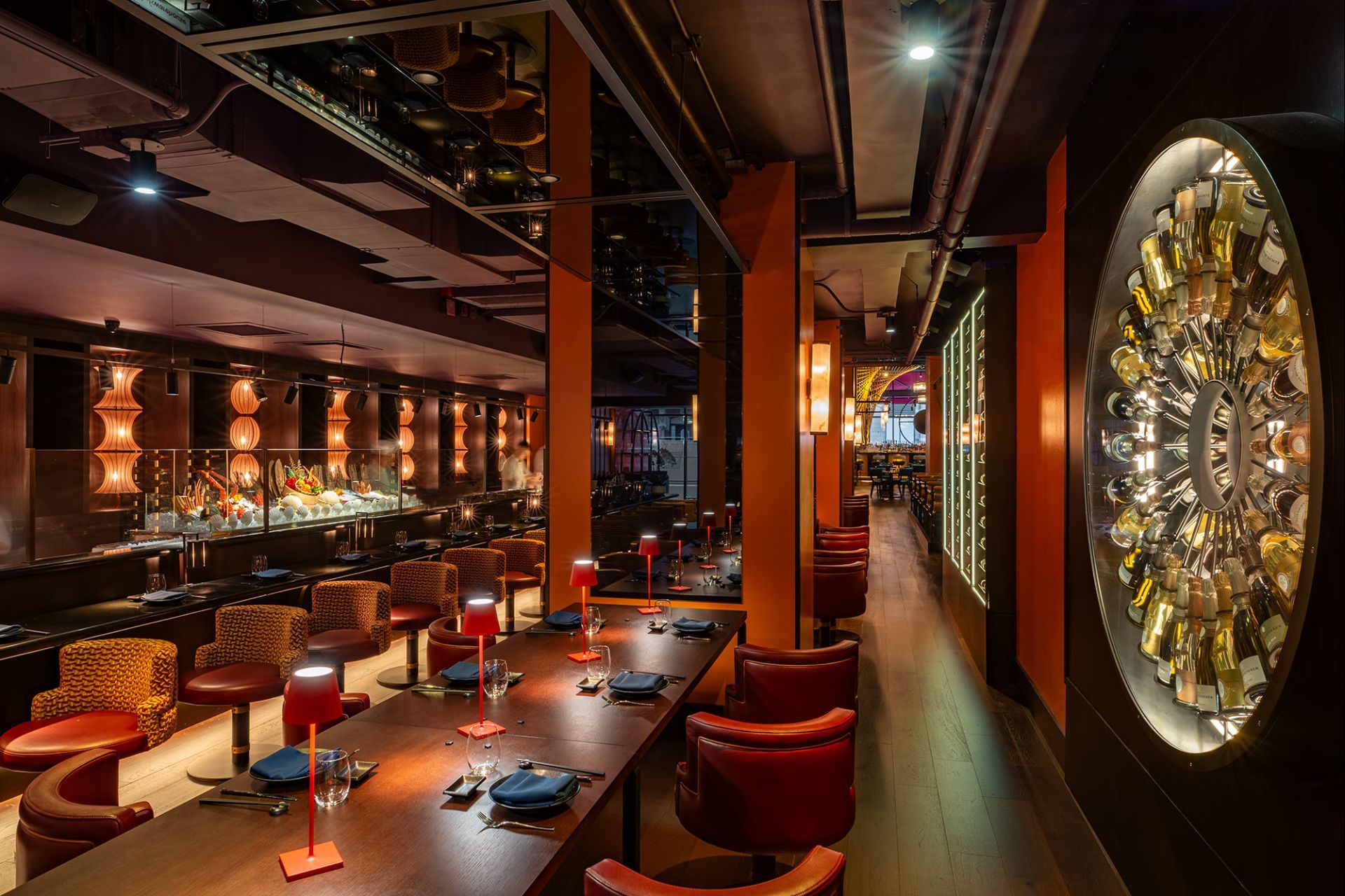 A dimly lit dining room with a seafood display counter and a circular wall display of bottles.