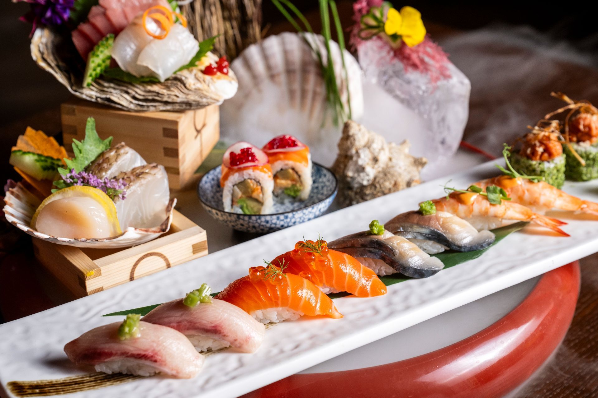 An assortment of sushi and sashimi including nigiri, a roll, scallops and shellfish on ice and shells.