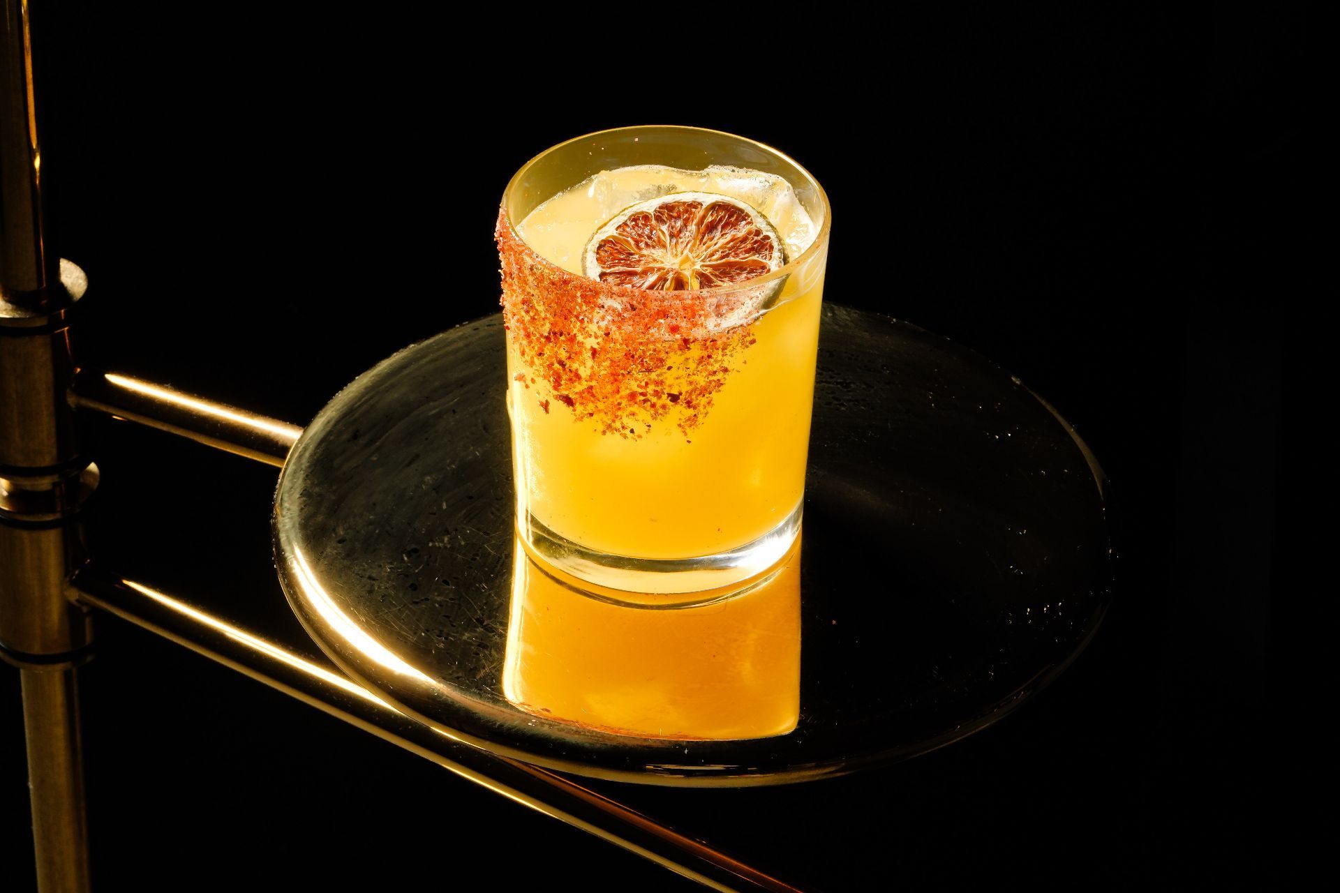 A cocktail with a chile-salt rim and a dried citrus wheel garnish.