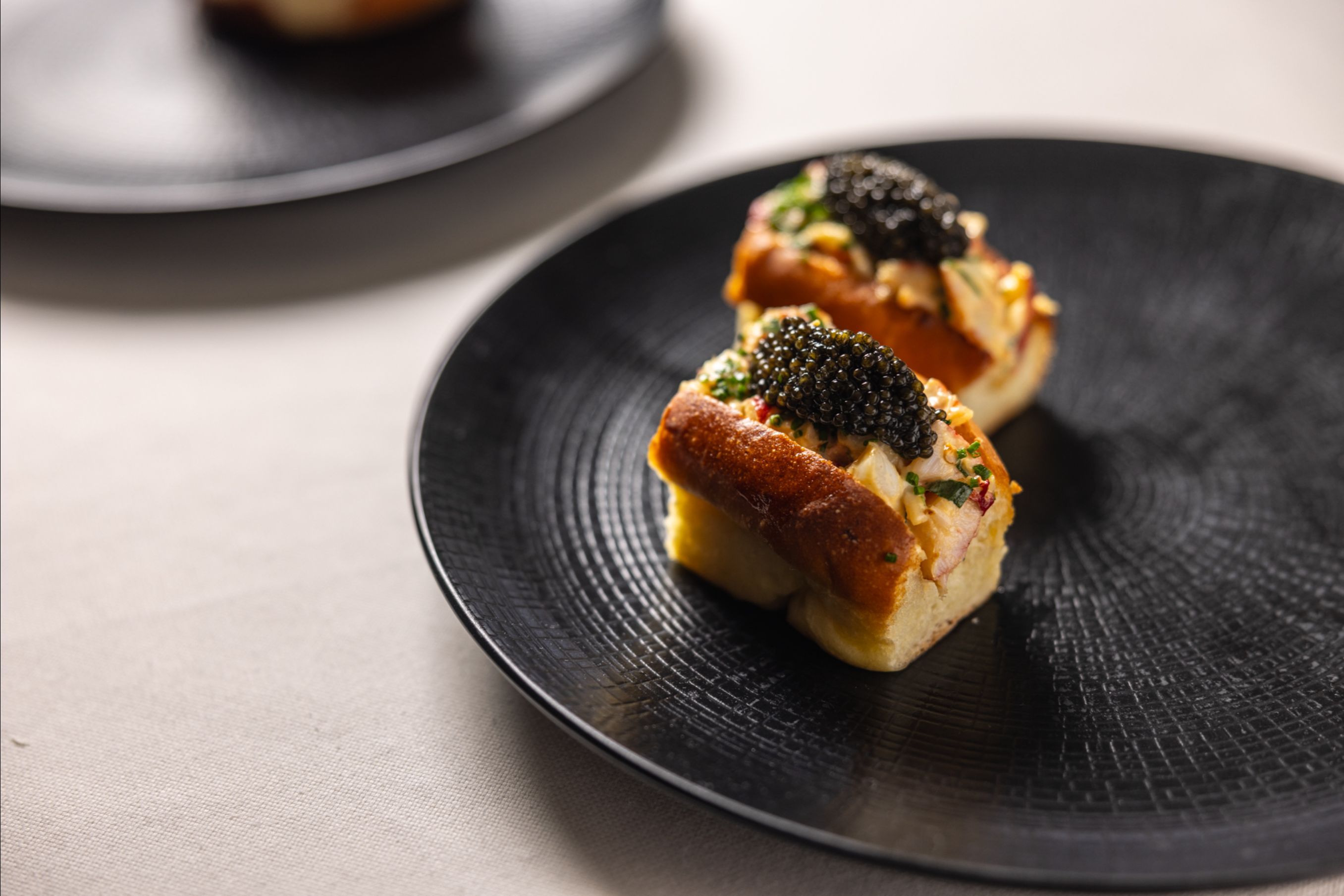 Two bread rolls topped with seafood salad and a mound of caviar on a dark plate.