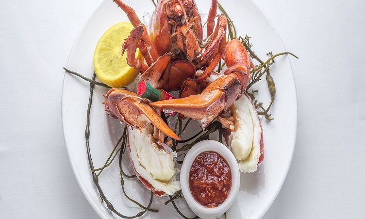 A plate of whole crab with claws, lemon and a small cup of sauce.