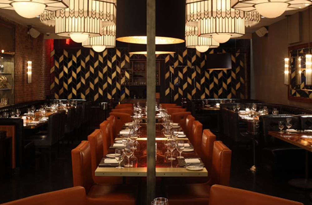 A dining room with orange leather banquettes, patterned dark walls and pendant lights over set tables.