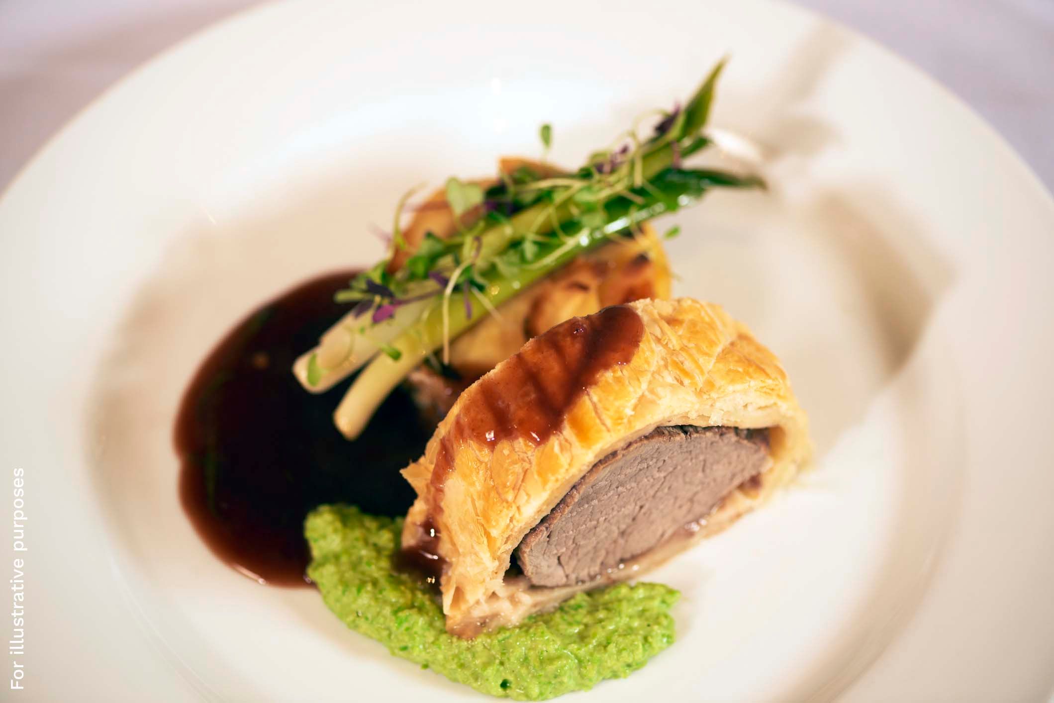 A pastry-wrapped meat dish sliced open to show the pink centre, plated with asparagus, microgreens, a pea puree and a dark sauce.