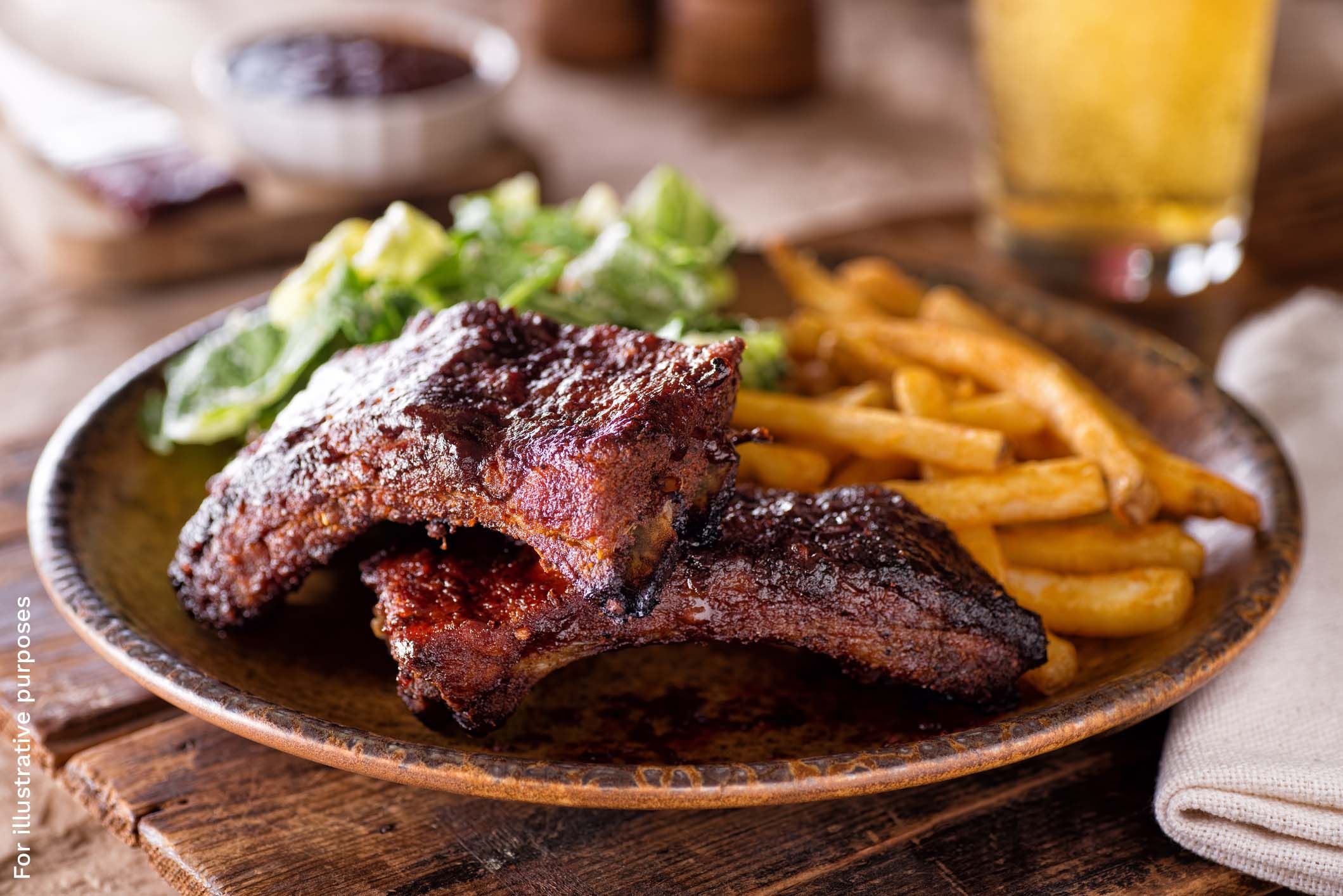 Barbecue ribs with a charred glaze served with fries and a green salad, alongside a glass of beer.